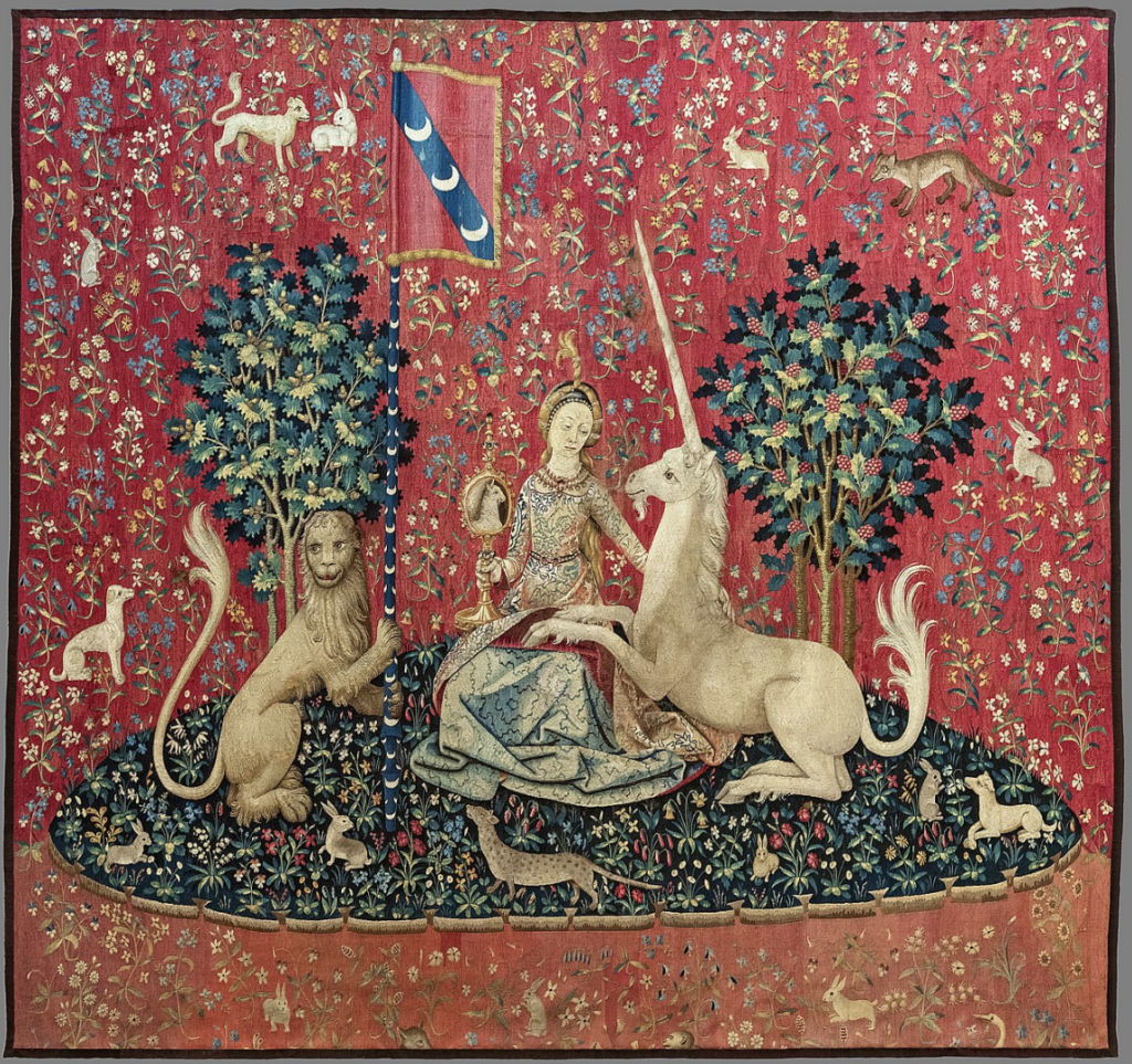 On a red tapestry, a woman sits on a hill between a lion and a unicorn. The unicorn has its front legs resting in her lap and she is reaching to touch it and looking at it. The lion is holding a flag.