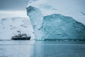 A ship passes by an iceberg off the coast of Greenland. Photo by Hubert Neufeld on Unsplash