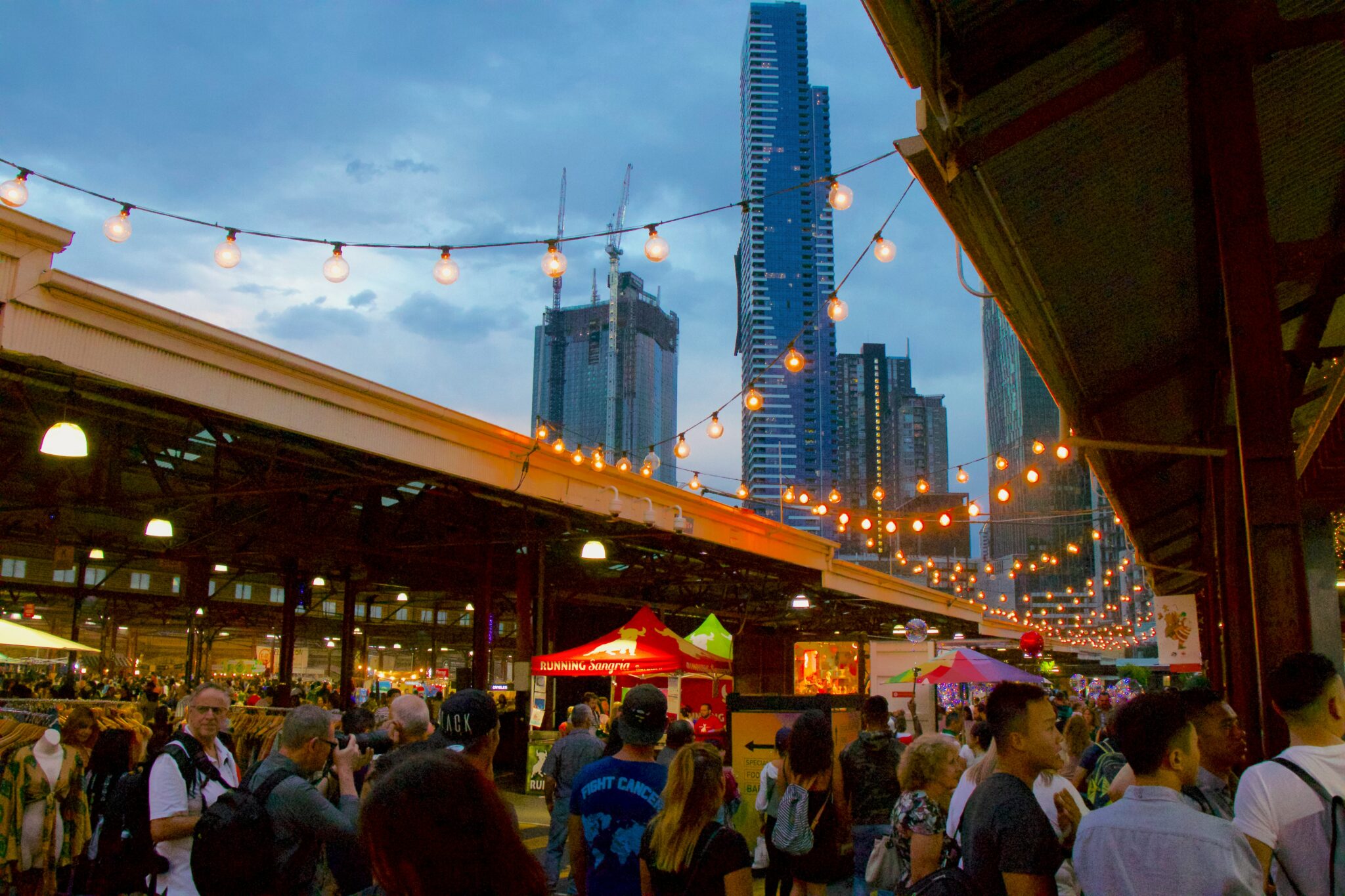 People browse a night market in the foreground while high rise towers are visible behind them. Photo by Mitchell Luo on Unsplash.